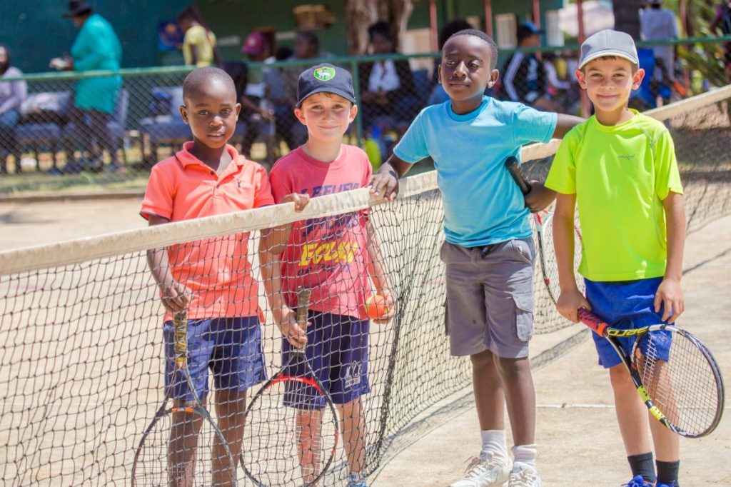 kids playing tennis doubles and socializing. 