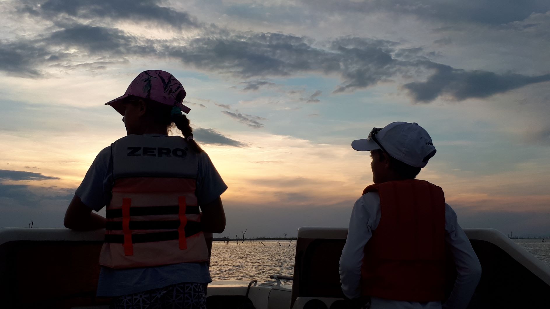 Children driving the boat at sunset.